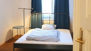 Une chambre à coucher avec un lit, une lampe sur pied, une chaise et une fenêtre avec des rideaux.