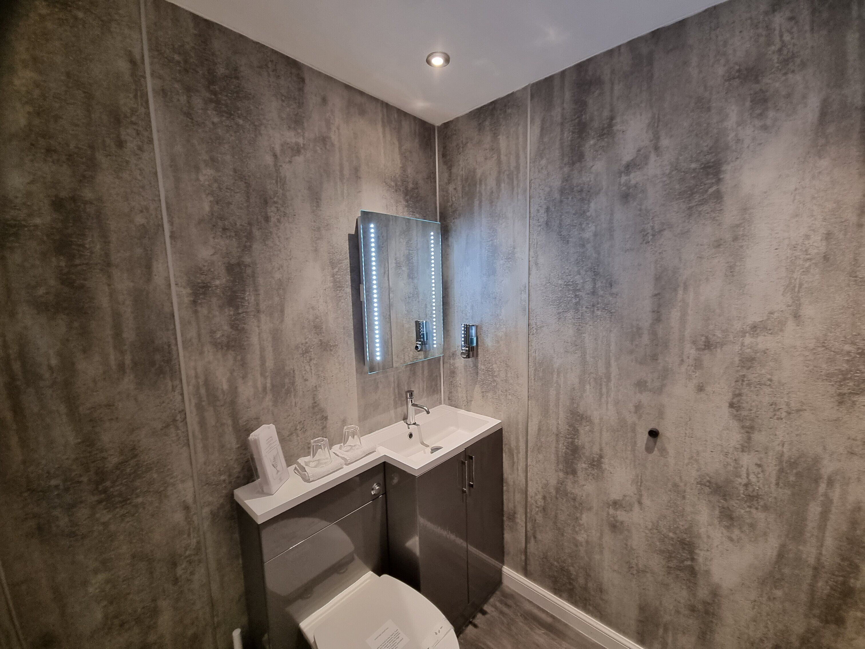 A bathroom with a modern design, featuring a large mirror, a sink, and a toilet.