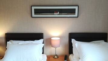 A hotel room with two beds, a nightstand with a lamp, a remote control, and a framed picture on the wall.