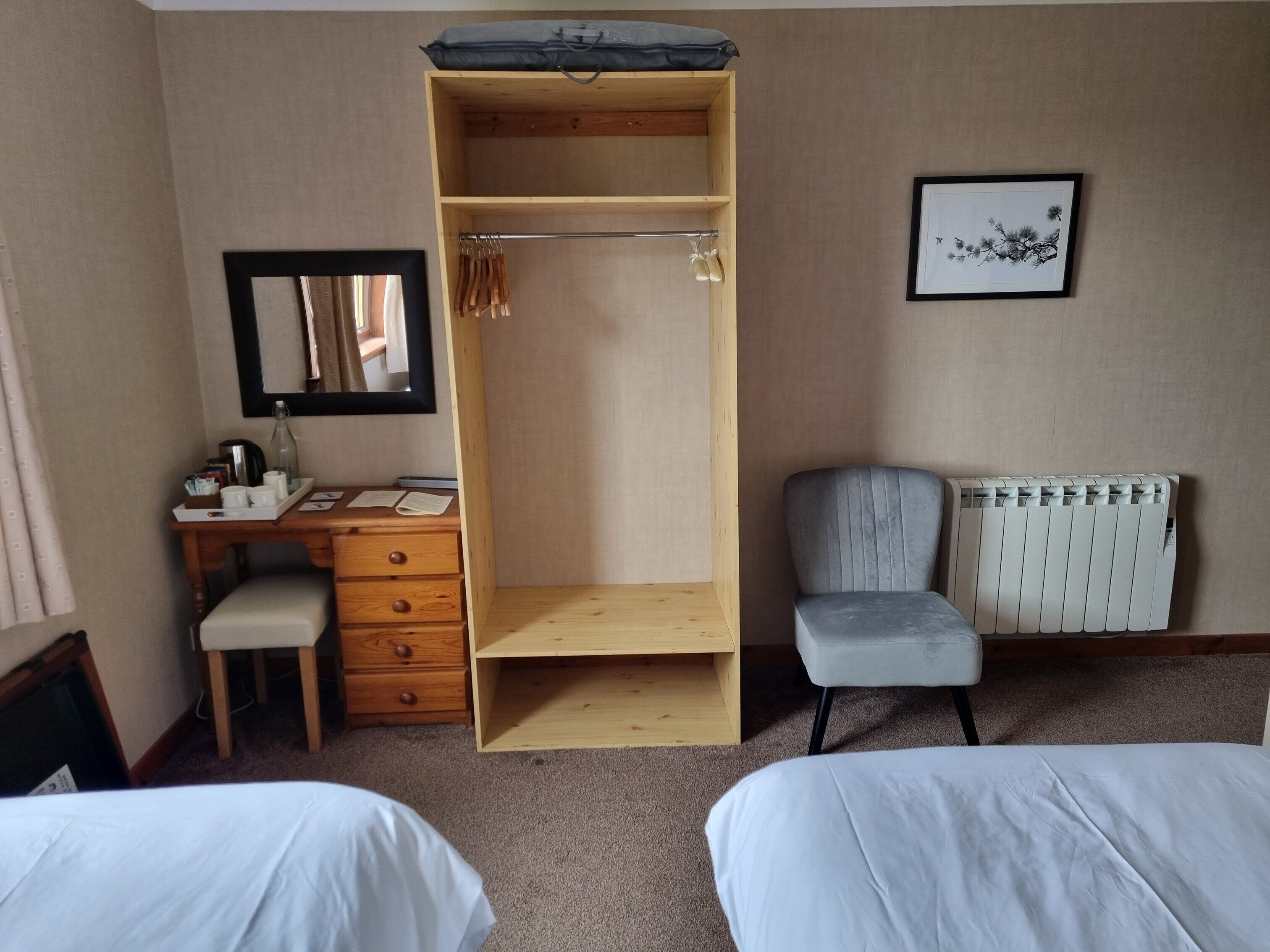A bedroom with a wooden wardrobe, a desk with a chair, a radiator, and two beds.