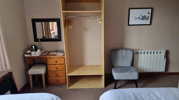 A bedroom with a wooden wardrobe, a desk with a chair, a radiator, and two beds.