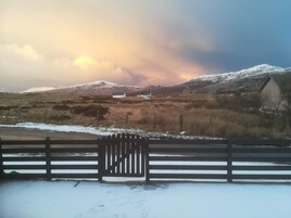 Paisaje rural con un campo nevado, una valla de madera y una casa de fachada blanca.