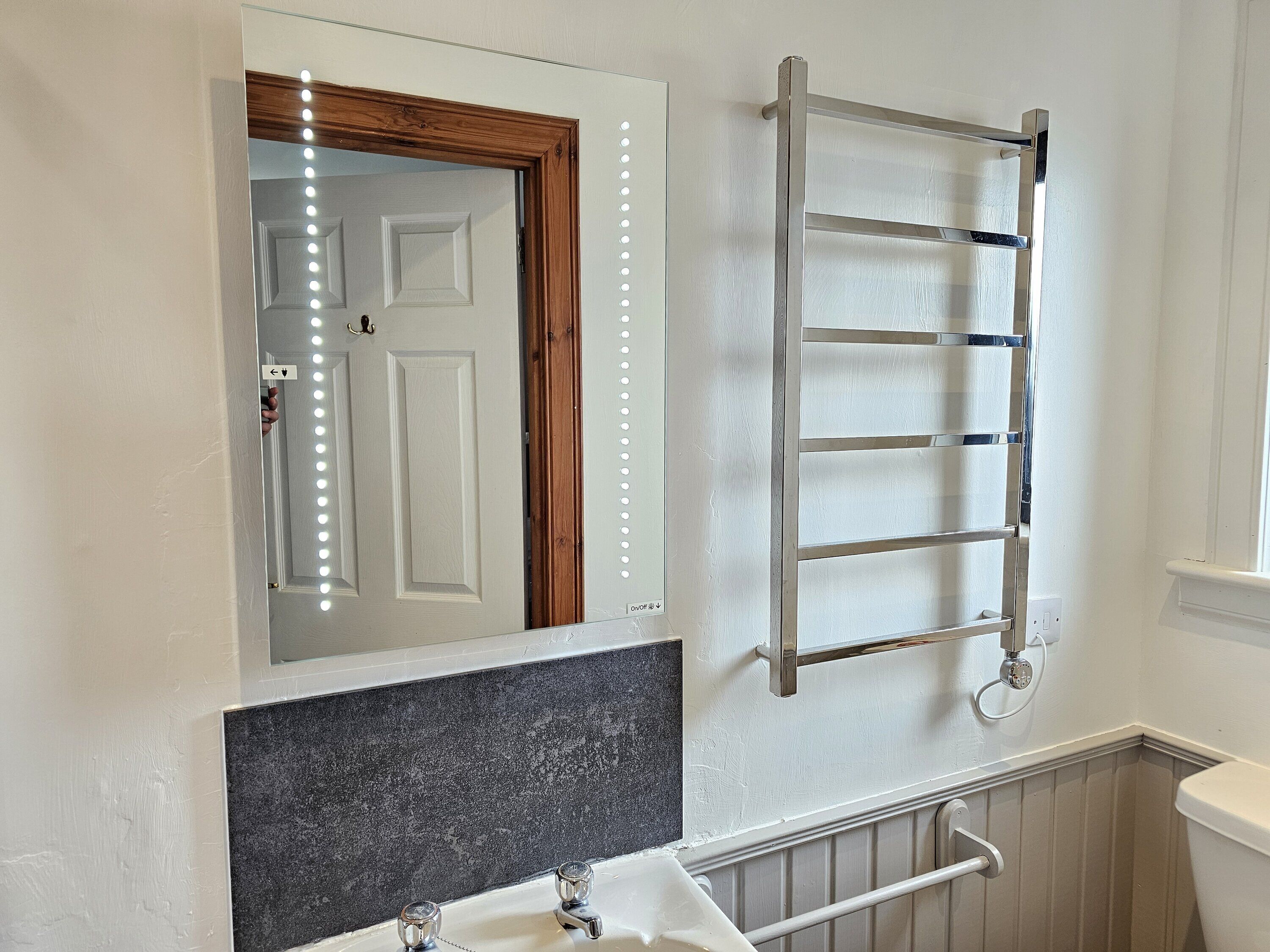 A bathroom with a mirror, vanity, sink, towel rack, and a door with lights.