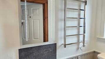 A bathroom with a mirror, vanity, sink, towel rack, and a door with lights.