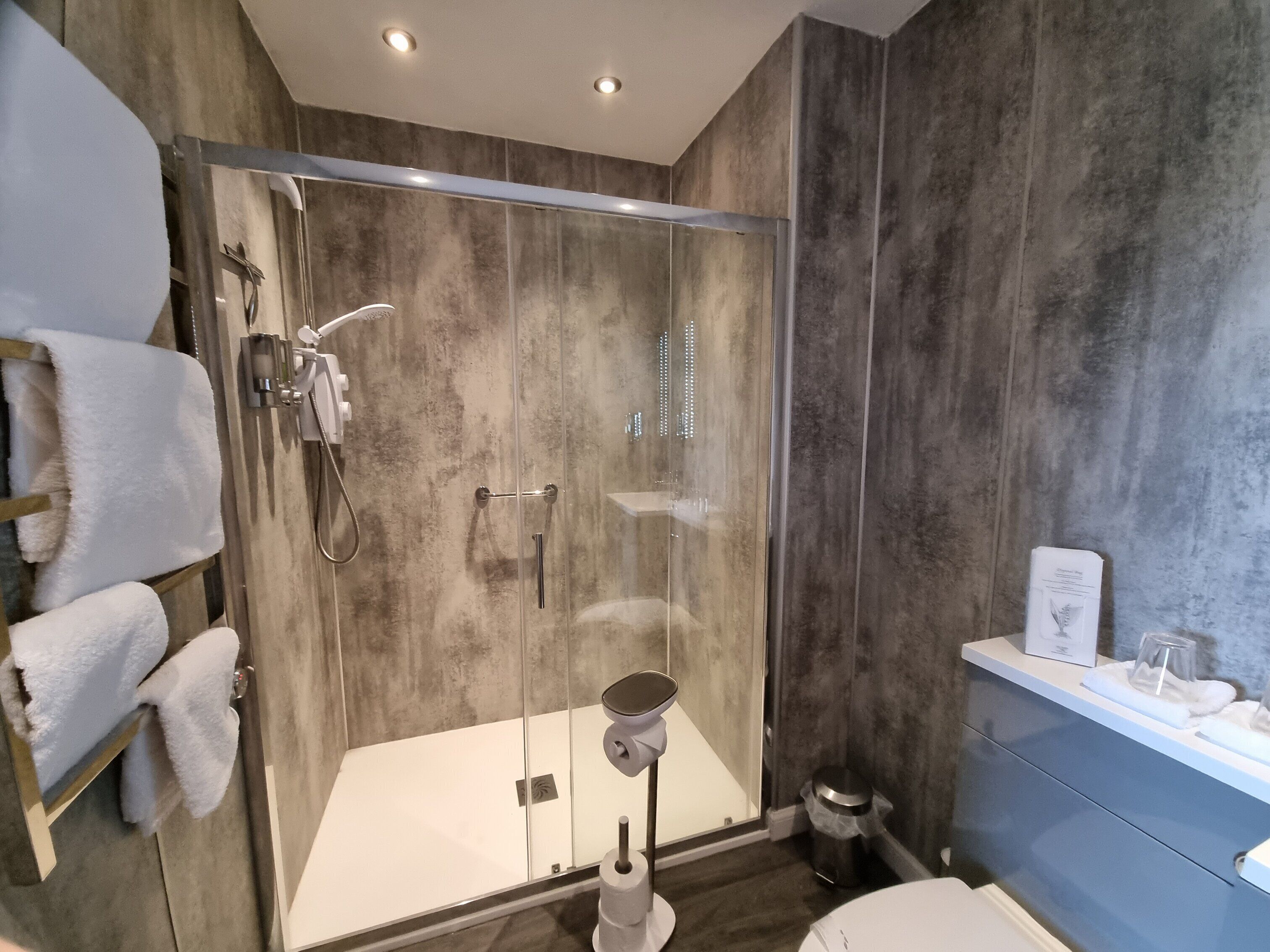 A modern bathroom with a glass-enclosed shower, a white sink, and a blue vanity.