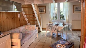 Una sala acogedora con una escalera de madera, una mesa de comedor lista para dos personas y un sofá.