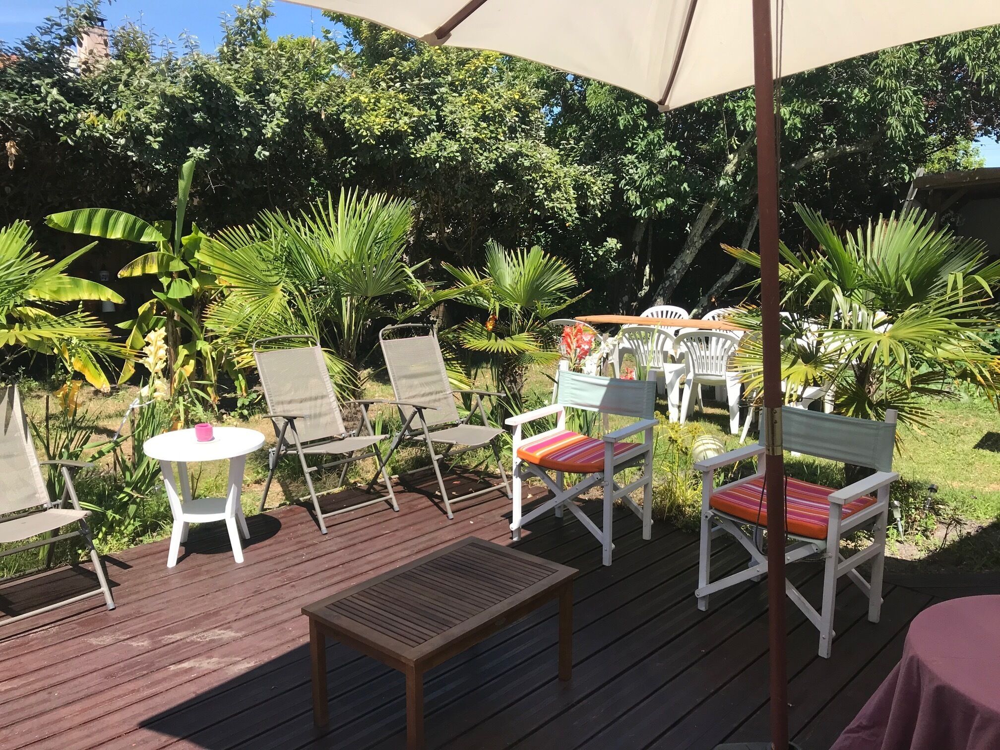 An outdoor patio area with white folding chairs, a wooden table, and a large umbrella providing shade.