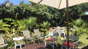 Un patio al aire libre con sillas plegables blancas, una mesa de madera y un paraguas grande que da sombra.