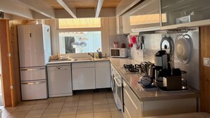 Cocina moderna con electrodomésticos blancos, vigas de techo de madera y vistas al exterior.