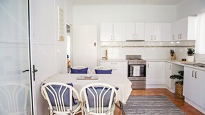 Una cocina moderna con armarios blancos, horno empotrado y comedor con mesa y sillas.