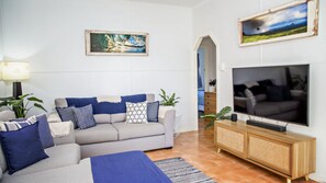 Un salon avec un canapé gris, des coussins bleus, un téléviseur et un tableau accroché au mur.
