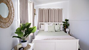 A bedroom with a bed, curtains, a bedside plant, a lamp, and a mirror.
