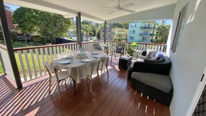 A covered outdoor area with a table set for dining, chairs, a sofa, and a ceiling fan.