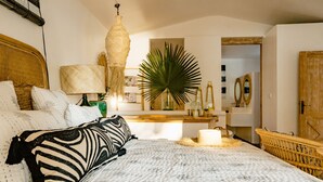 Een slaapkamer met een groot bed, een nachtkastje, een hanglamp, een spiegel en een deur.
