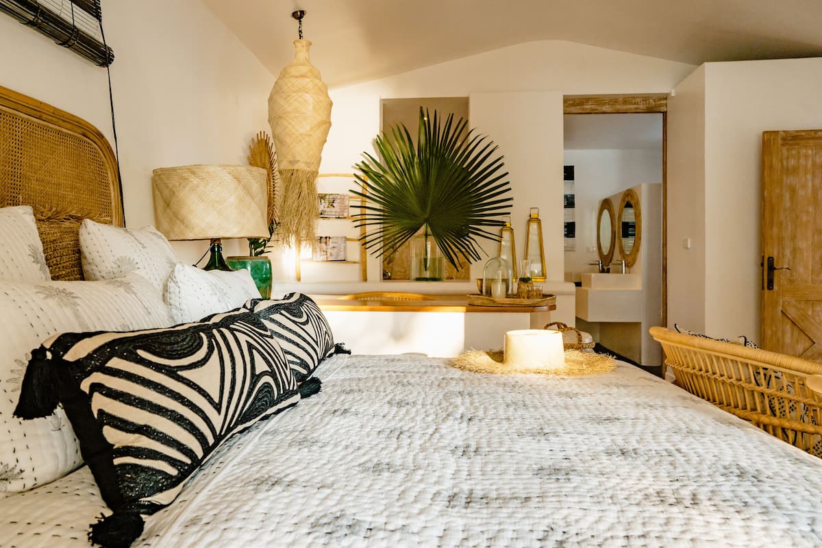 A bedroom with a large bed, a bedside table, a hanging lamp, a mirror, and a door.