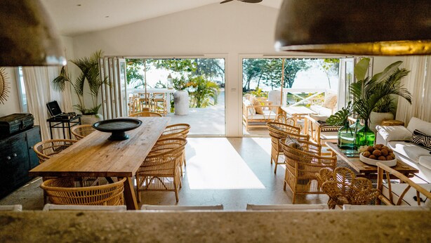 Een ruime woonkamer met een houten eettafel, rieten stoelen en uitzicht op de omgeving.