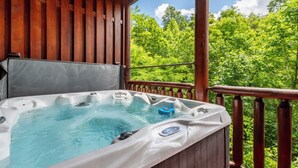 A hot tub on a wooden deck with a view of a forest.