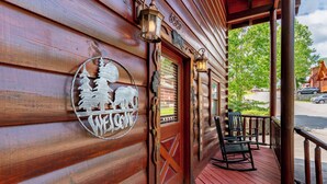 A wooden cabin with a 'WELCOME' sign, a porch with chairs, and a view of the beach.