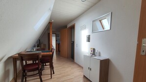 Un couloir étroit mène à un coin repas où se trouvent une table et des chaises en bois, un buffet blanc et un plafond doté d’une lucarne.