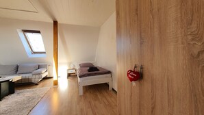 Une chambre avec un lit en mezzanine, un puits de lumière, une armoire en bois et un coin salon confortable avec un canapé et une table.