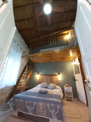 Un dormitorio con cama, cabecera, mesita de noche y espejo, con una escalera que sube a un nivel superior.