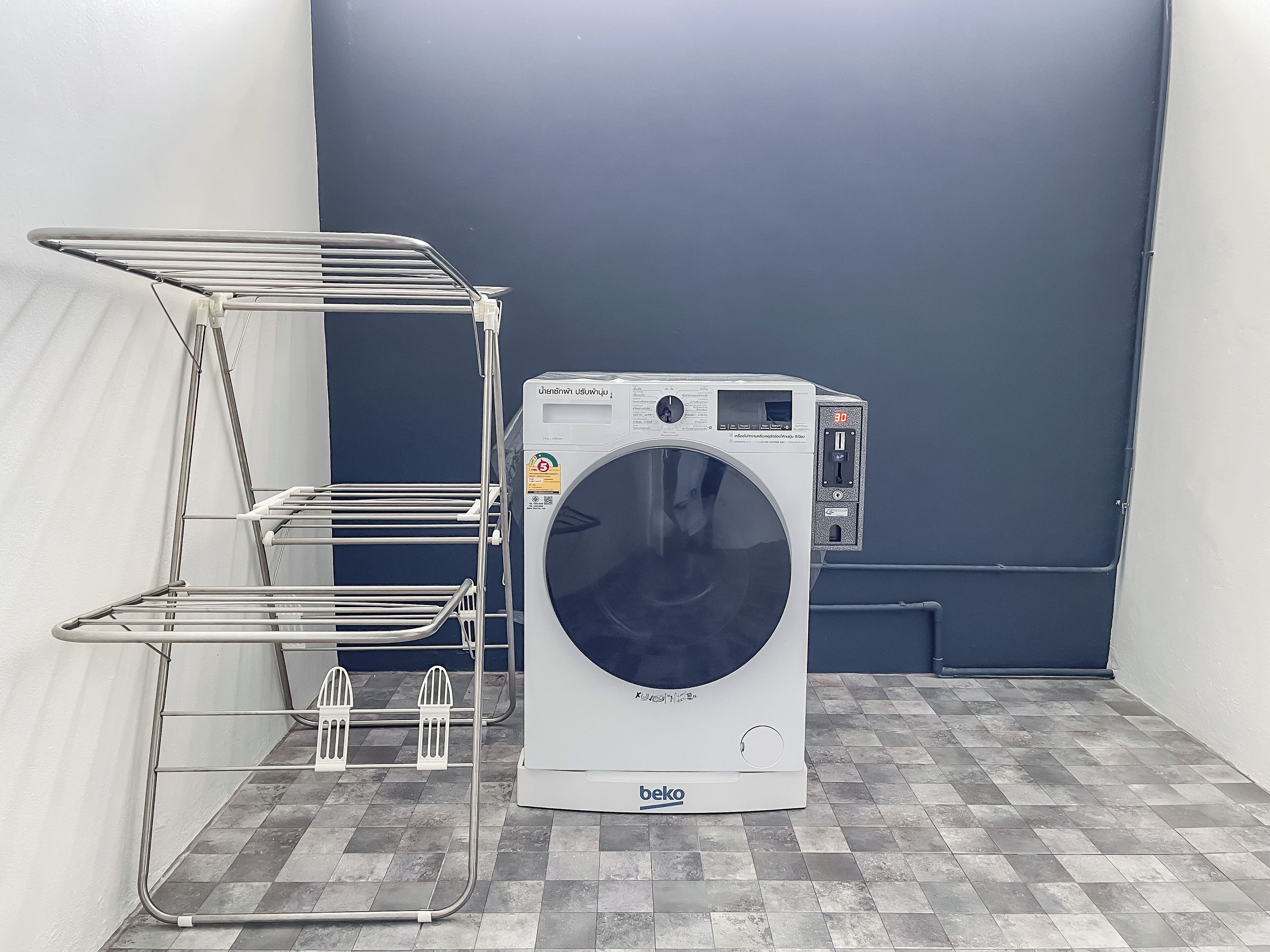 A front-loading washing machine with a control panel, a metal drying rack, and a tiled floor.