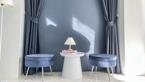 A modern room with a large window, two blue upholstered chairs, a white side table with a lamp, and a magazine on the table. - Shapel Hostel and Cafe (Chiang Mai)