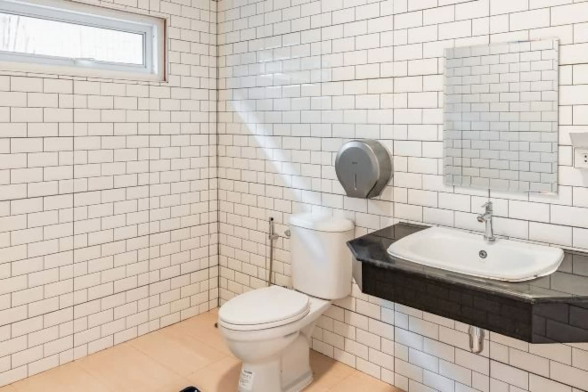 A bathroom with white tiled walls, a white toilet, a black sink, and a mirror above the sink.