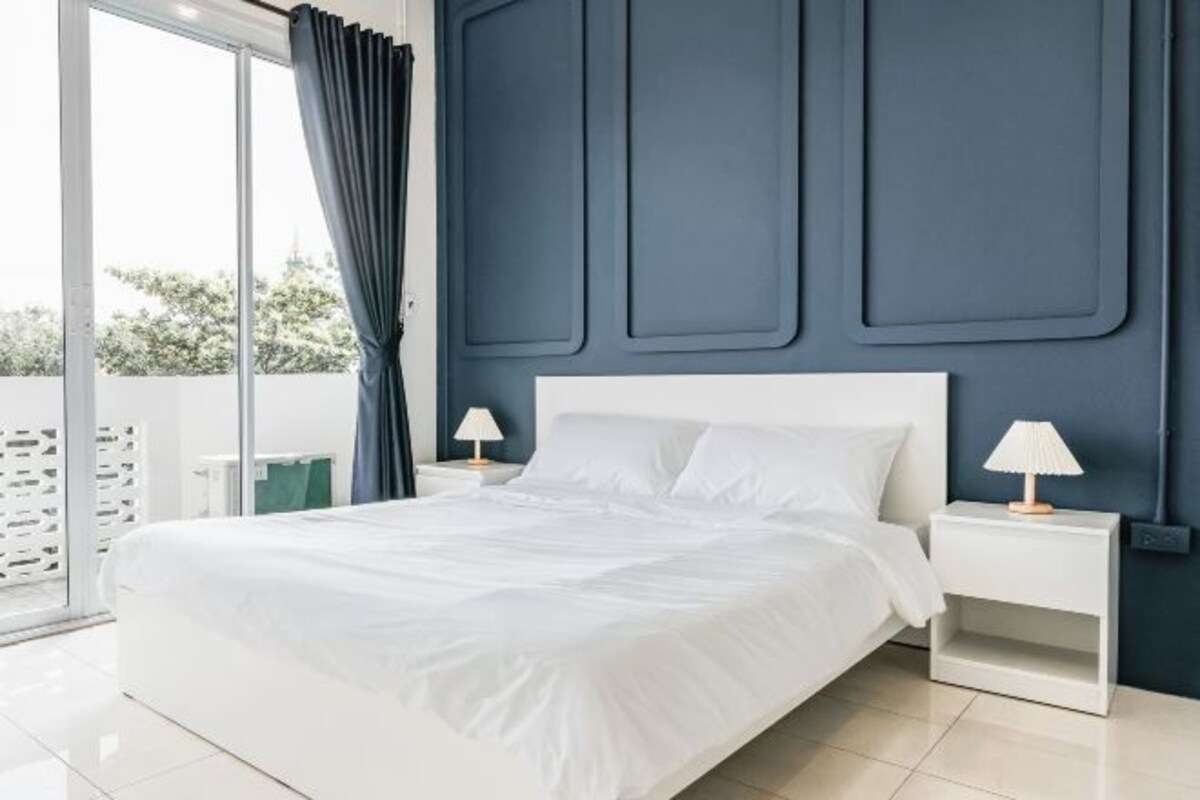 A modern bedroom with a large bed, white bedding, two bedside tables with lamps, and a dark blue accent wall.