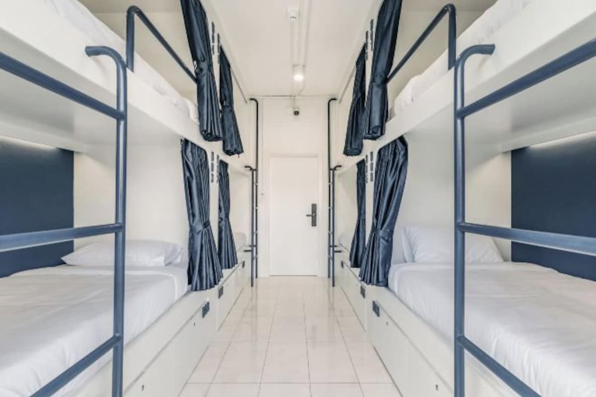 A corridor with bunk beds on either side, a white door at the end, and a tiled floor.
