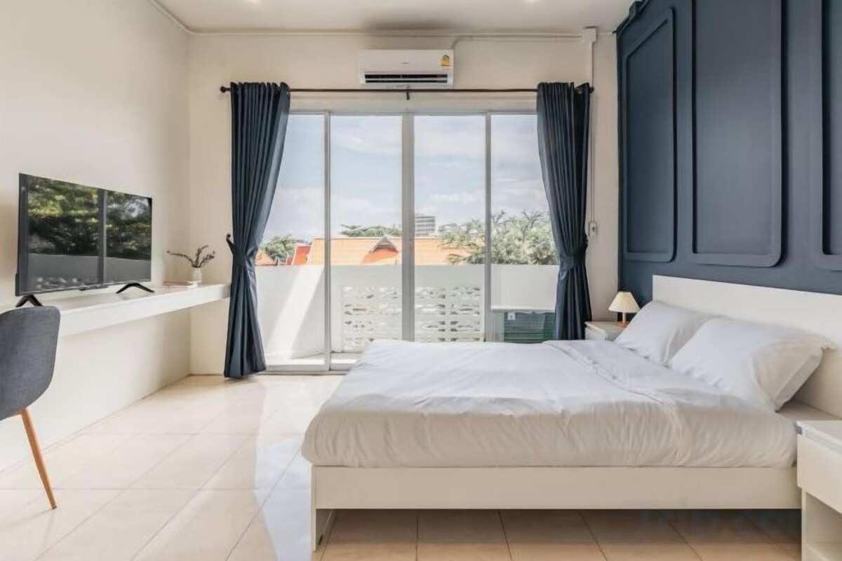 Un dormitorio moderno con una cama, televisión, escritorio y ventana con cortinas.