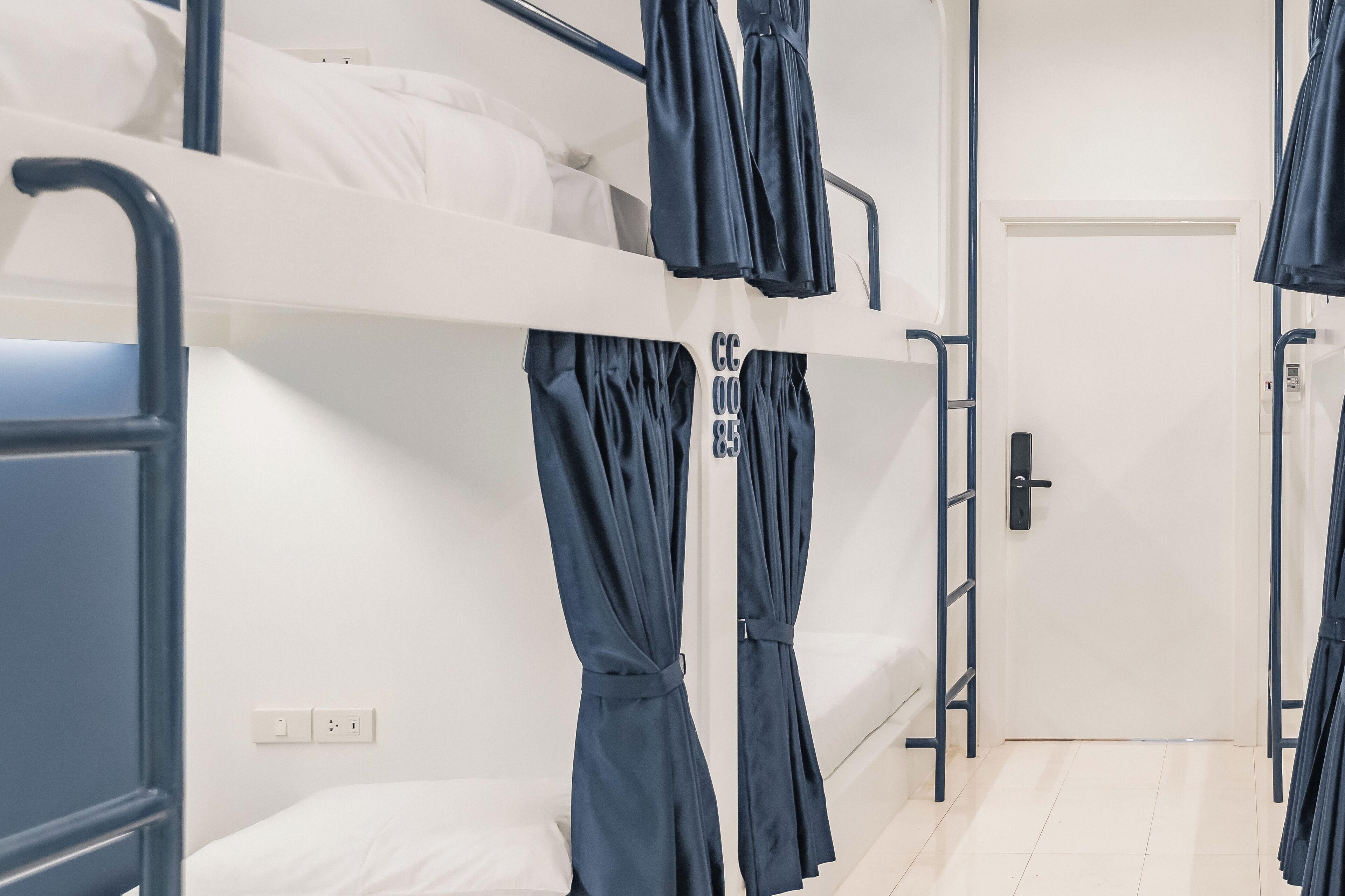 Ein Schlafraum mit Etagenbetten, einer weißen Wand, einer Tür und einer Steckdose.