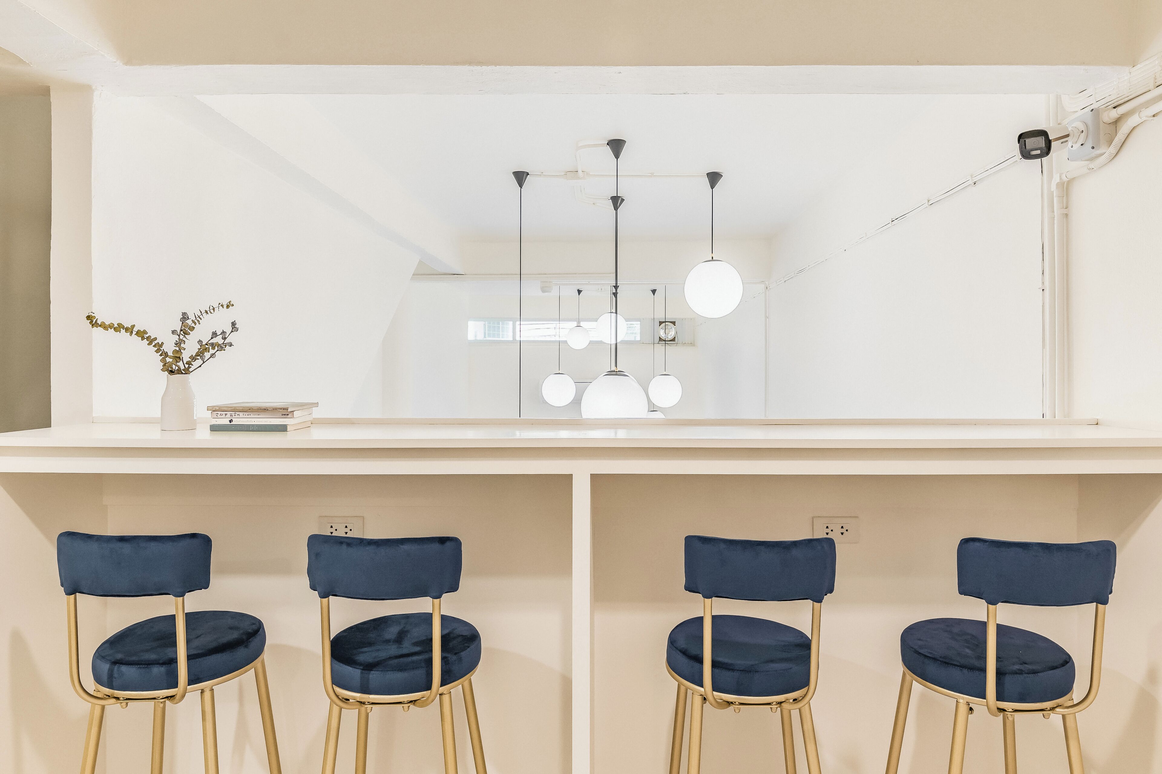 A modern room with a white ceiling, a white desk, and three blue chairs with gold legs.