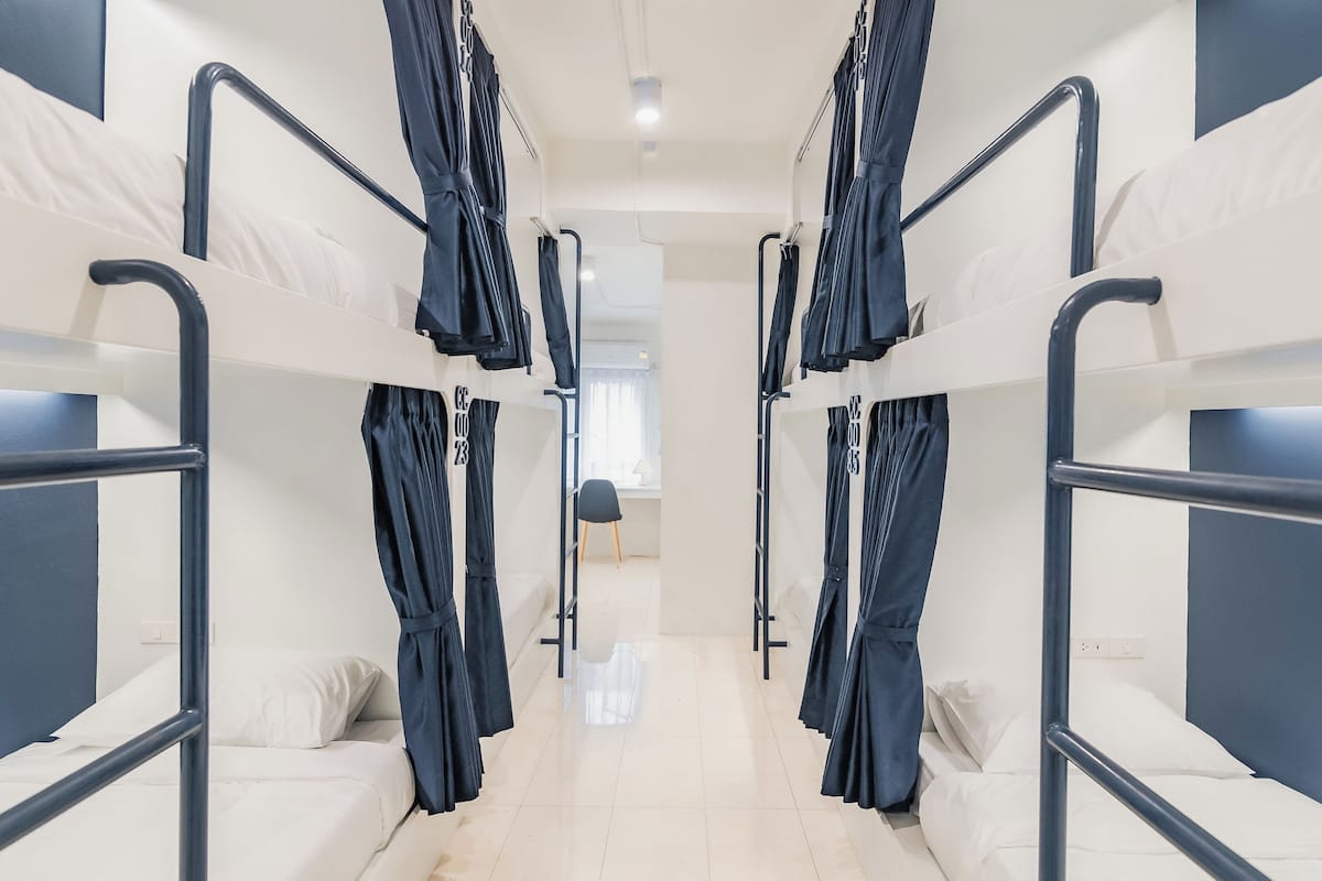 Un pasillo con literas, cada una con una escalera de metal negro y ropa de cama blanca.
