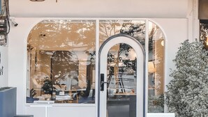 The exterior of ShaPel Hostel x Café with a large arched window, a signboard, and a potted plant to the right. - Shapel Hostel and Cafe (Chiang Mai)