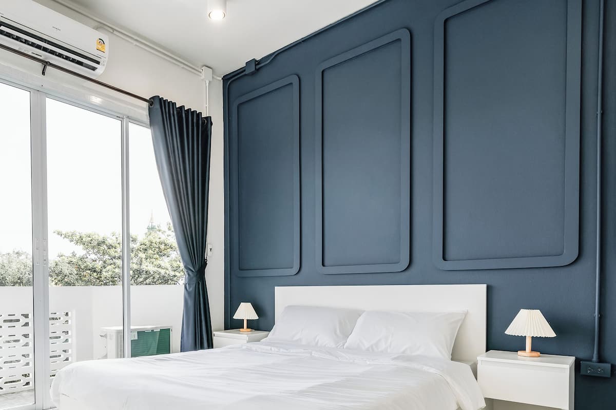 Un dormitorio moderno con una cama grande, dos mesitas de noche con lámparas, una pared de acento oscura y vistas a través de un ventanal corredero.