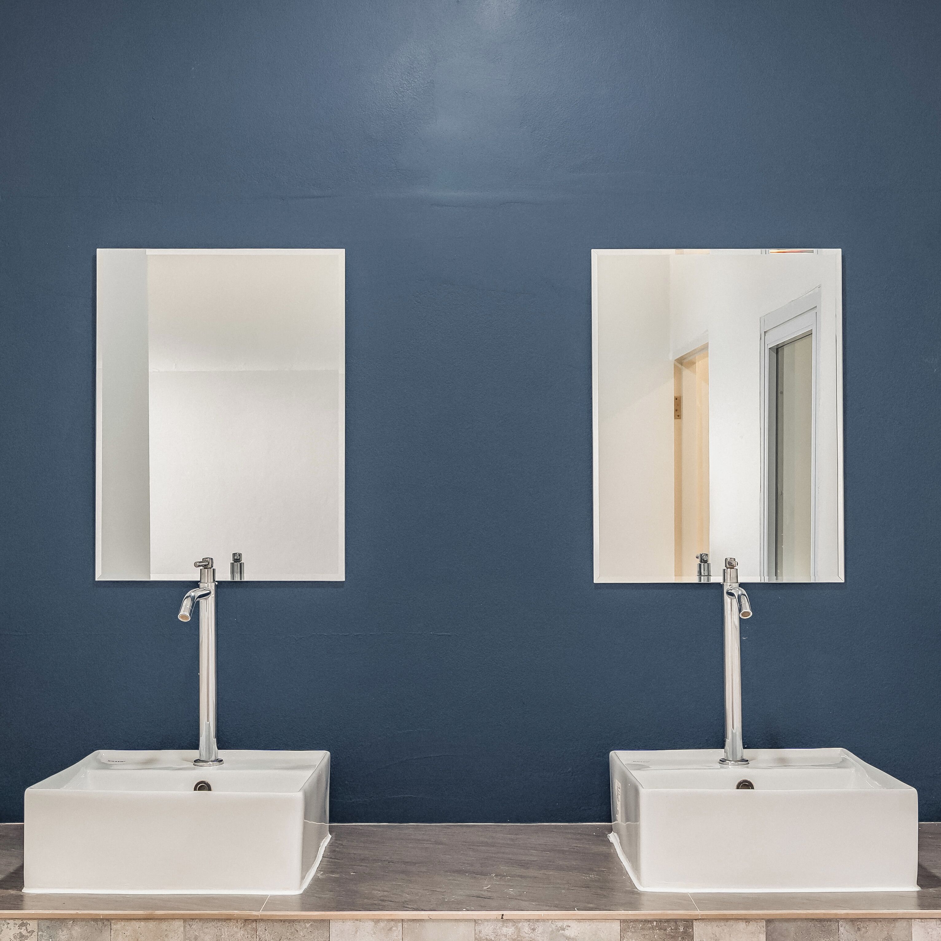 Two white sinks with chrome faucets and mirrors above them, set against a dark blue wall.