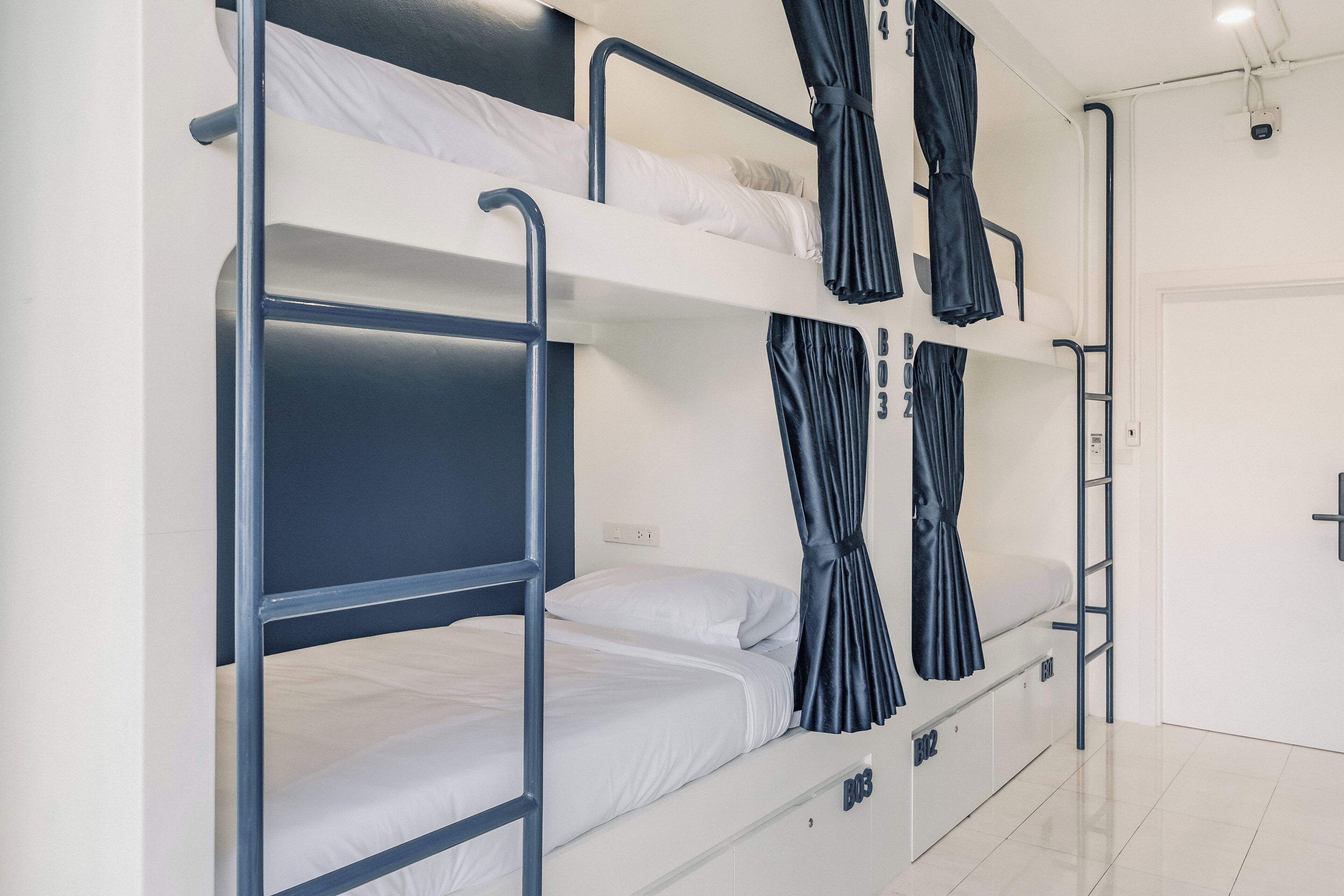 Une chambre avec un lit superposé, un mur blanc, une porte et une fenêtre avec des rideaux.
