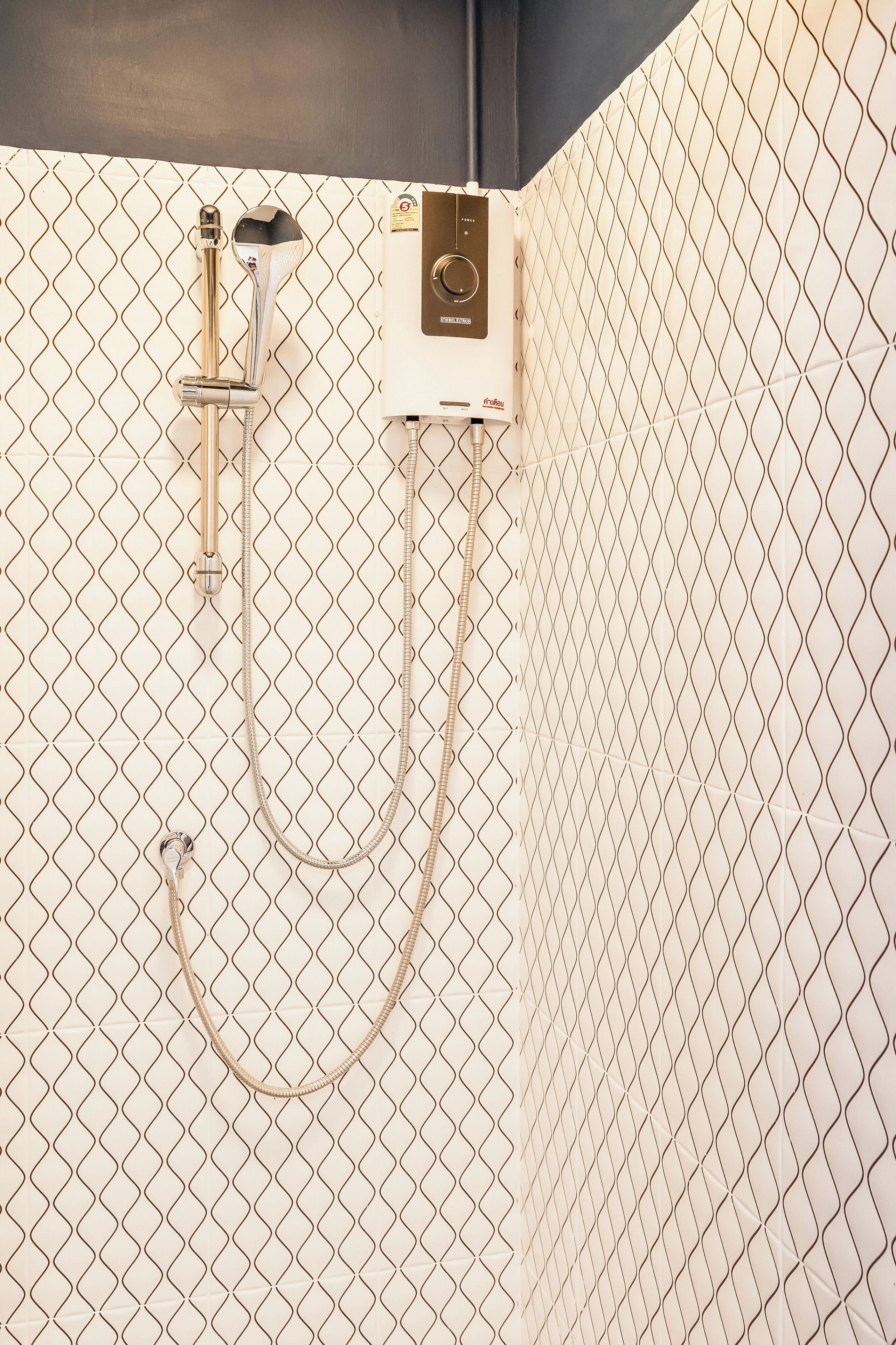 Un área de ducha con un cabezal y panel de control montados en una pared cubierta de azulejos.