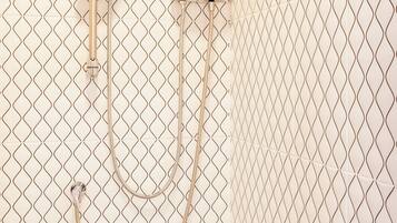 Un área de ducha con un cabezal y panel de control montados en una pared cubierta de azulejos.
