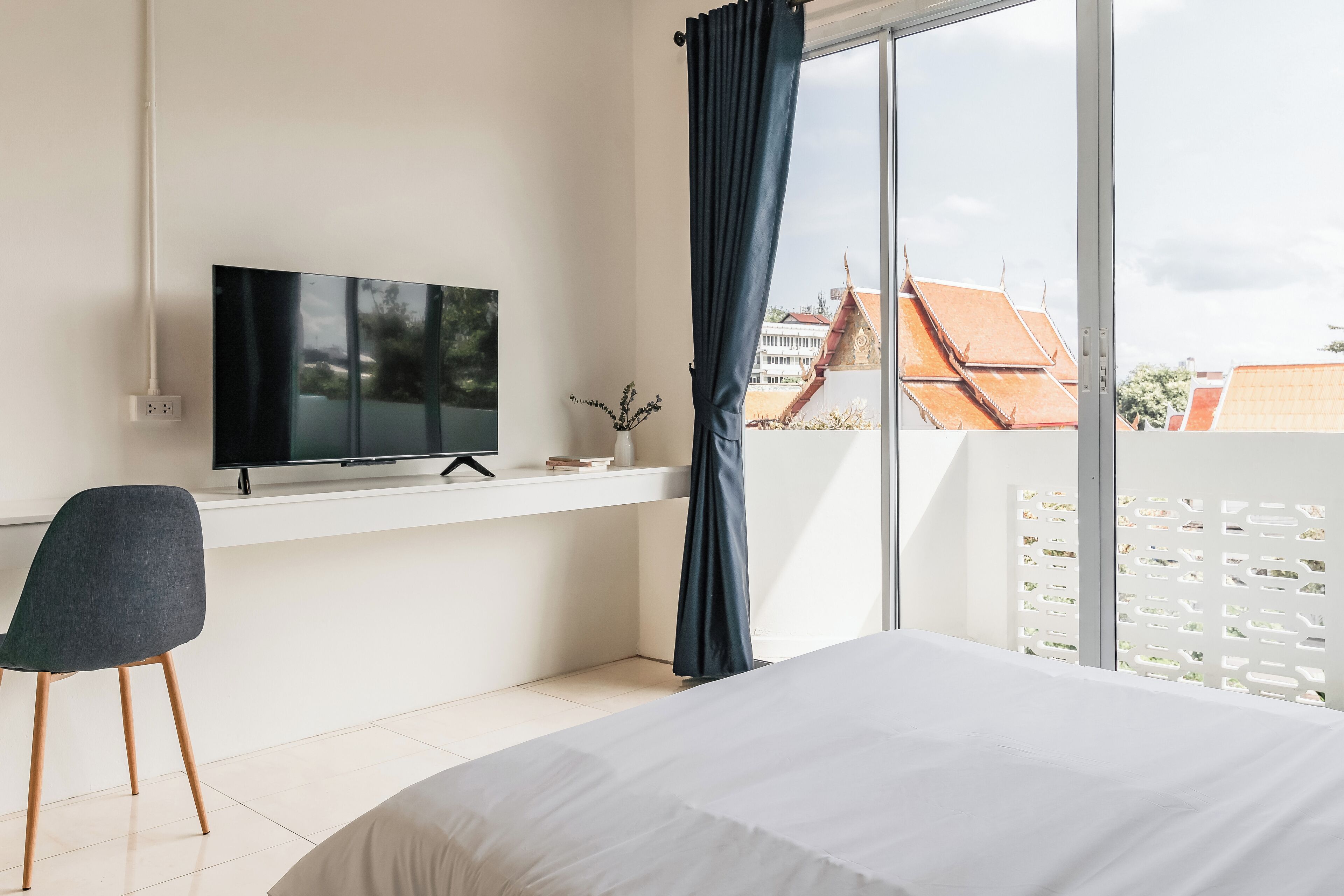 Habitación de hotel moderna con una cama grande, un televisor de pantalla plana montado en la pared, un escritorio con una silla y un balcón con vistas a edificios.