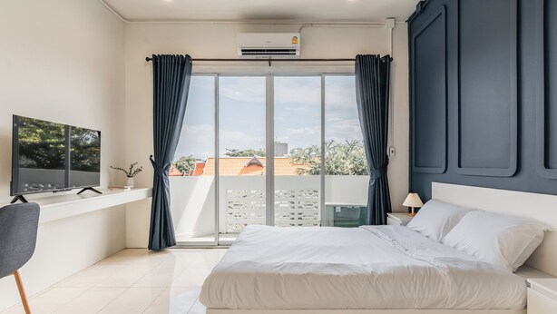 A modern bedroom with a large bed, a TV on a stand, and a view of buildings through the window. - Shapel Hostel and Cafe (Chiang Mai)