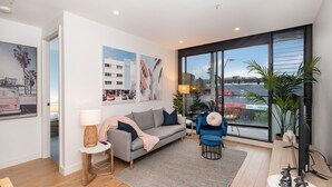 A modern living room with a grey sofa, a small round table, and a large window offering a view of the city.