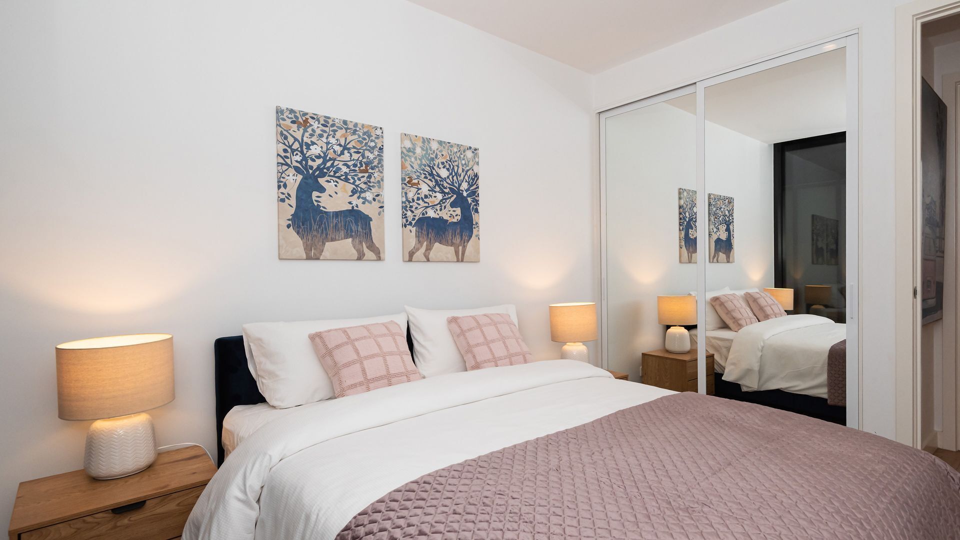 Une chambre à coucher comprenant un lit, deux lampes de chevet, une table de nuit, un grand miroir et deux œuvres d’art mural.