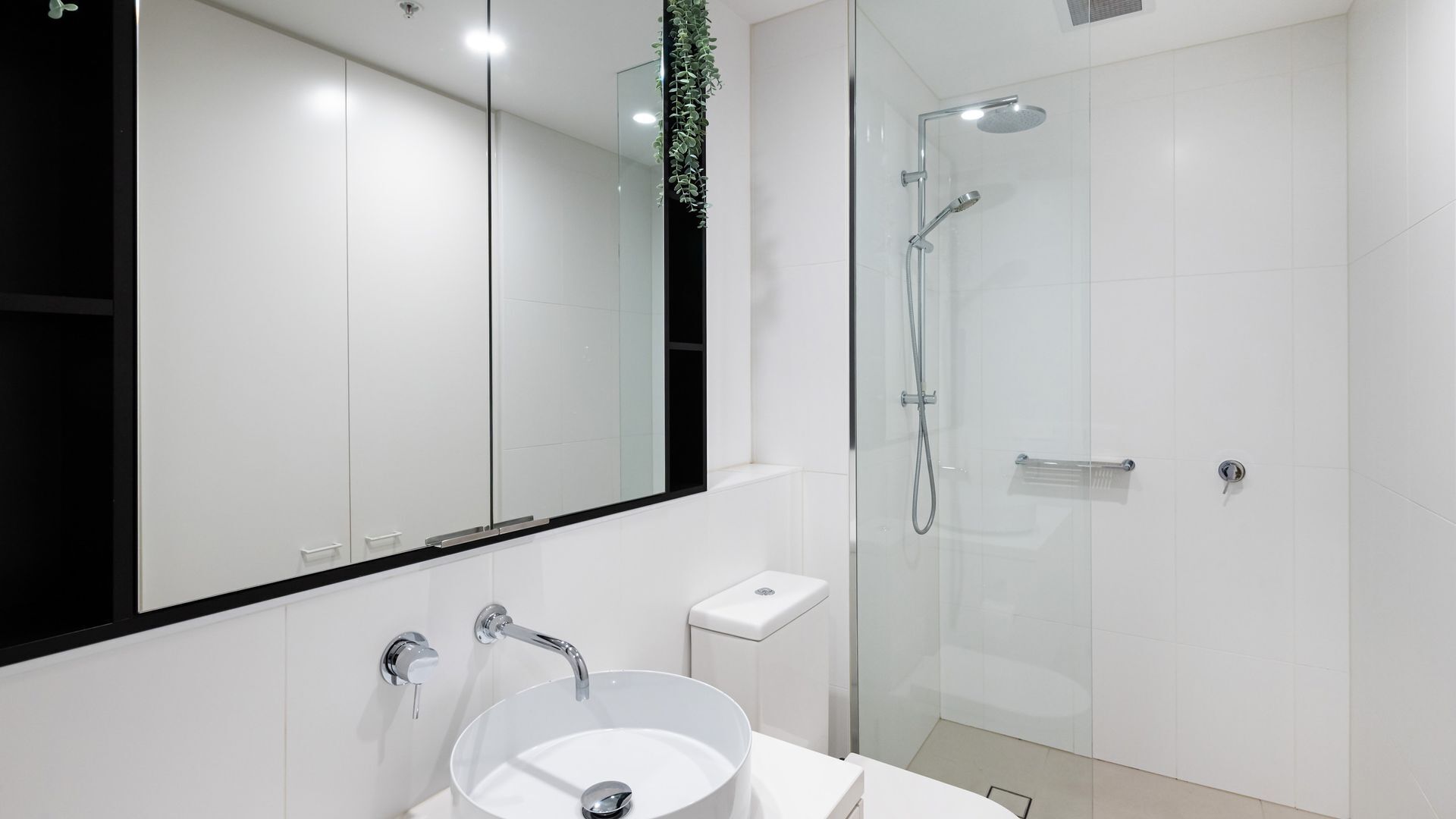 Une salle de bain moderne avec un lavabo blanc, une douche en verre et un grand miroir.