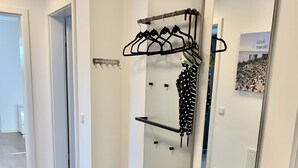 Käytävällä on naulakko, penkki ja peili, johon heijastuu juliste.