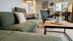 Moderni olohuone, jossa on vihreä sohva, samanvärinen nojatuoli, puinen sohvapöytä ja lattiavalaisin.