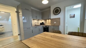 Moderni keittiö, jossa on harmaat kaapit, puinen ruokapöytä ja seinällä oleva kello.