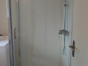 A glass-enclosed shower with a handheld showerhead and a wall-mounted control panel.