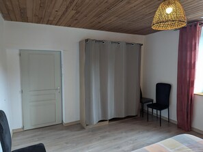 A room with a wooden ceiling, a bed, a chair, a curtain, and a door.